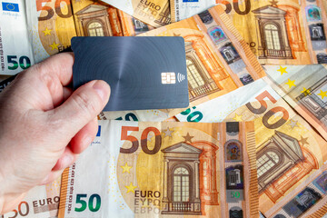 A woman's hands holding a gray credit card and in the background fifty euro bills scattered...