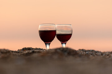 Two glasses of wine in the sand on the seashore. Sunset