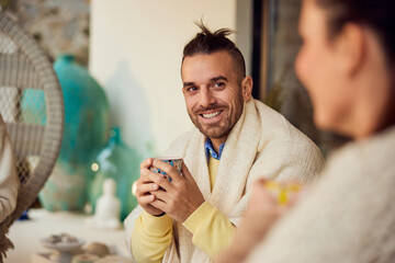 Focus on the smiling male talking to his female friends, holding a cup of coffee, sitting outdoors,...