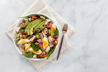 A freshly made tossed salad topped with chicken, avocado and egg.