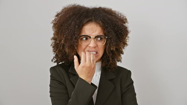 Anxious hispanic woman with curly hair looking worried, biting nails, overwhelmed by stress, standing against a stark white isolated background.