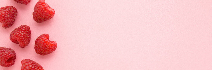 Fresh red raspberries on light pink table background. Pastel color. Wide banner. Closeup. Top down...