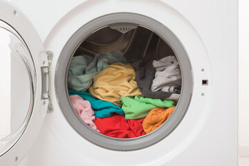 White opened washing machine full of colorful clothes. Closeup. Front view.