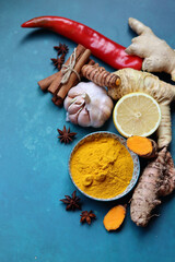 Homemade remedy ingredients top view photo. Ginger, lemon, cinnamon, anise, chili pepper, turmeric, ginger root, garlic bulb and spices on a blue background with space for text. 