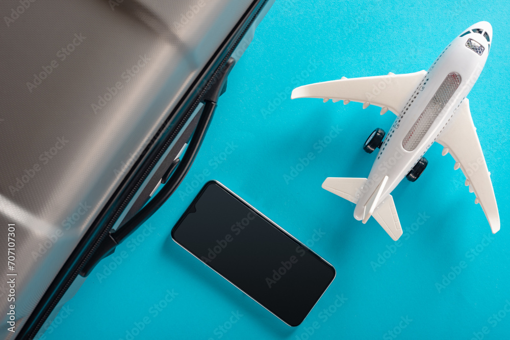 Wall mural flight suitcase with smartphone and model of airplane isolated on blue background