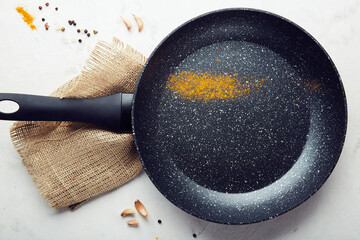 Black non-stick stainless steel frying pan with turmeric, garlic, pepper on a marble background....