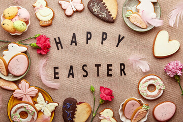Spring background with text Happy Easter. Aesthetic pastel spring Easter cookies, pink flowers and eggs flat lay.