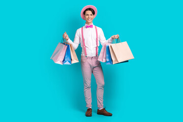 Full body photo of satisfied nice guy wear white shirt pink headwear bow tie holding shopping bags isolated on blue color background