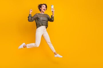 Fototapeta na wymiar Photo of overjoyed excited girl wear trendy clothes going empty space talking video call isolated on yellow color background
