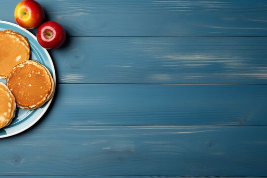  The pancakes are on a light blue plate with two apples on a blue wooden background. a place for a text or recipe.