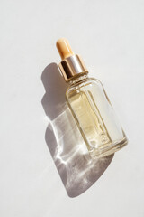 Serum with collagen and peptides in transparent glass bottle on light background with sunlight shadow