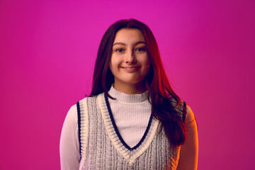 Fototapeta premium Young woman with long brunette hair, dressed casual outfit smiling looking at camera against gradient pink background. Concept of human emotions, self-expression, fashion and style. Ad