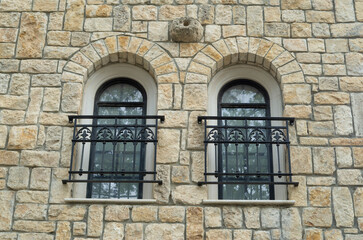 Two arched windows  with black wrought iron window railings on stone wall
