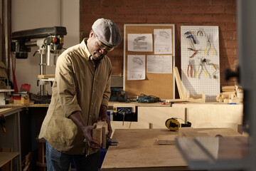 Black senior man as skilled craftsman setting up equipment in sunlit woodworking shop