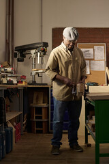 Vertical portrait of African American senior man as skilled carpenter standing in sunlit workshop