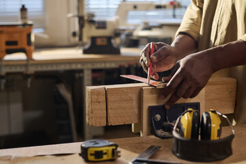 Side view closeup of senior carpenter measuring wood and building furniture in sunlit workshop - obrazy, fototapety, plakaty