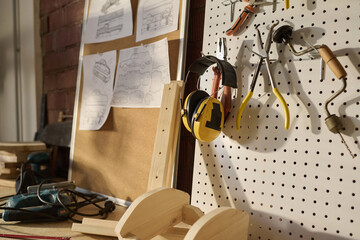 Close up of protection headphones and various tools on pegboard in carpenters workshop, copy space