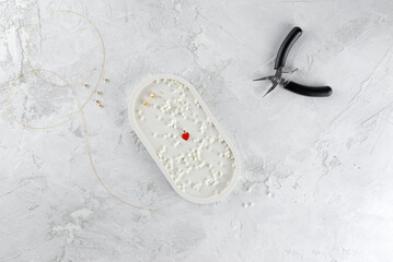 Making jewelry from mother-of-pearl beads in a plate on a light background.