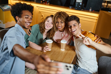 happy african american man taking selfie with trendy multiethnic students in hostel cafe, friendship