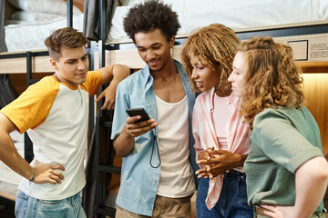 youthful african american man using smartphone near multicultural buddies in students hostel