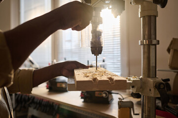 Close up of unrecognizable carpenter drilling wood using machine tool in workshop with sunlight