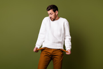 Photo of confused nice man wear stylish clothes spend money showing empty pockets isolated on khaki color background