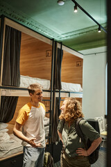 cheerful and young couple with backpacks talking in cozy room of students hotel, travelers