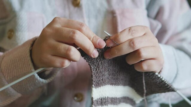 Female caucasian hands knitting brown wool scarf with knitting needles.