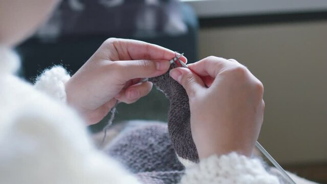 Female caucasian hands knitting brown wool scarf with knitting needles.