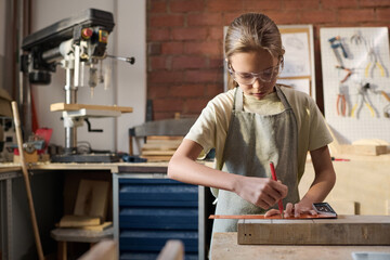 Waist up portrait of Caucasian girl measuring wooden board and building model in carpenting workshop