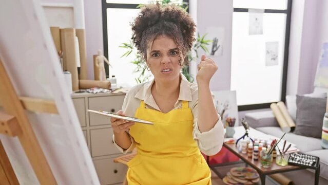 Furious hispanic artist with curly hair, a woman's rage in the studio