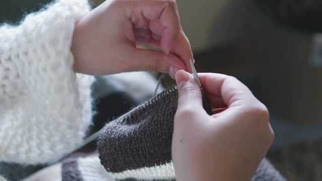 Female caucasian hands knitting brown wool scarf with knitting needles.