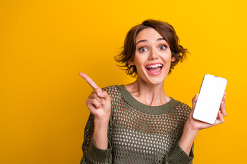 Photo portrait of lovely young lady hold device point empty space dressed stylish knitted khaki garment isolated on yellow color background