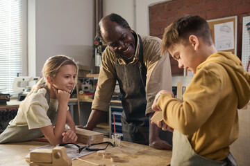 Portrait of smiling African American carpenter teaching children building wooden toys in workshop