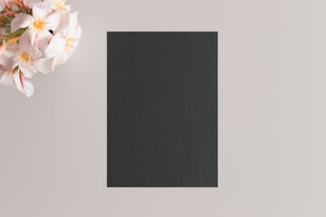 Black invitation card mockup with a oleander on the beige table. 5x7 ratio, similar to A6, A5.