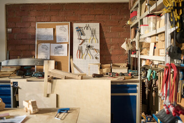 Wide angle view at carpentry workshop in sunlight with various tools and wooden models on table