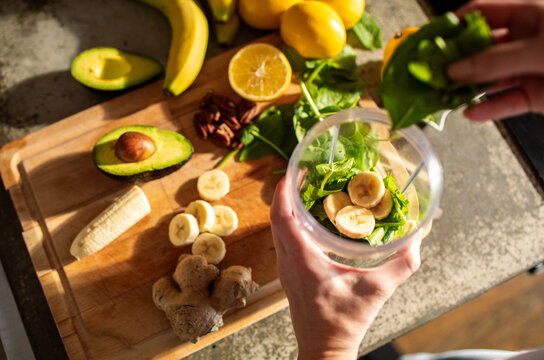 Woman preparing a healthy smoothie with fresh spinach, banana, avocado, and lemon