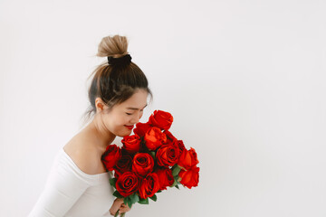 Asian woman holding red roses, Happy smiling and receiving  and looking at flowers on Valentines day, standing isolated over white background wall.