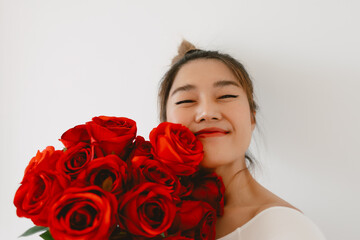 Asian woman holding red roses, Happy smiling and showing flowers, looking at camera, standing isolated over white background wall.
