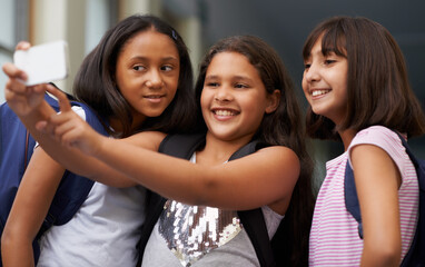 Obraz premium Elementary school friends, girls and selfie with smile for fun educational memory together. Diversity, young students and group of happy kids taking picture for social media, photography and learning