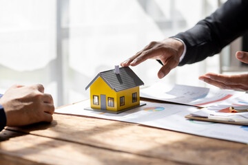 Real estate agents offer contracts to buy or rent housing. Businessman holding model small building house with property insurance at table in home sales office
 - obrazy, fototapety, plakaty
