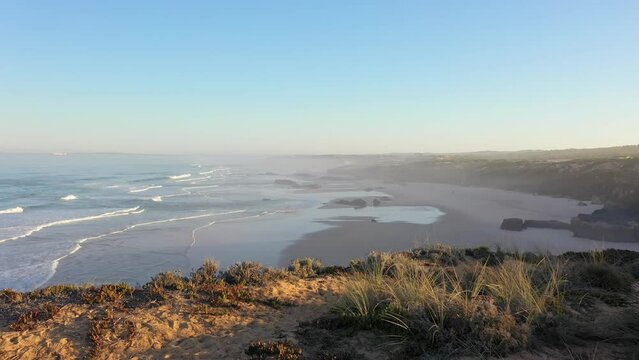 Aerial view of Praia do Malhao beach at sunrise with fog and haze in Portugal. flying over the shore of a rocky abyss