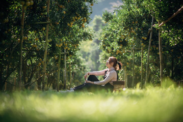 A happy woman farmer is resting in orchard or orange farm.