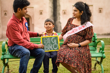 Indian couple posing for maternity baby shoot with their 5 year old kid. The couple is posing in a...