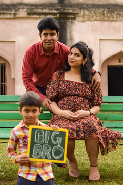 Indian couple posing for maternity baby shoot with their 5 year old kid. The couple is posing in a lawn with green grass and the woman is flaunting her baby bump in Lodhi Garden in New Delhi, India