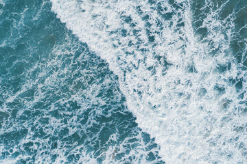 Aerial top view of white foam on the surface of the blue sea.