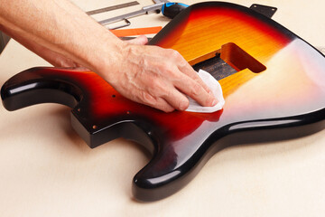 Guitar master polishes body of electric guitar.