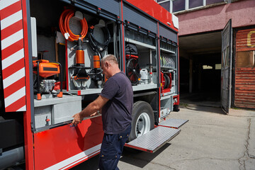 A dedicated firefighter preparing a modern firetruck for deployment to hazardous fire-stricken...