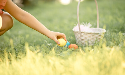 Little girl picking in basket colorful painted eggs on Easter egg hunt in park
