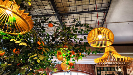 Yellow wicker chandeliers on the ceiling and orange tree with tangerines. Interior, room design,...
